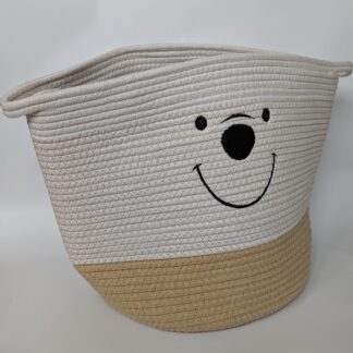 Bild på en korg gjord av bomullsrep med ett handtag på vardera sida. Korgen är vit och beige och har ett broderat ansikte av en björn på framsidan med ett stort leende och en svart nos.
